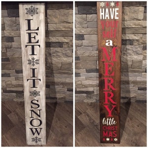 Puede incluir: Dos letreros de madera con mensajes navide&ntilde;os. El letrero de la izquierda es blanco con letras negras y copos de nieve que dicen "Let It Snow". El letrero de la derecha es marr&oacute;n con letras rojas que dicen "Have Yourself a Merry Little Christmas".