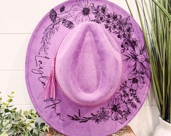 May include: A purple felt fedora hat with a black floral design and the name "Layla Ann" written on the brim.