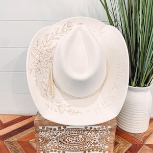 May include: A white cowboy hat with a floral design and the text "A.K. 18.06.2014" on the brim.
