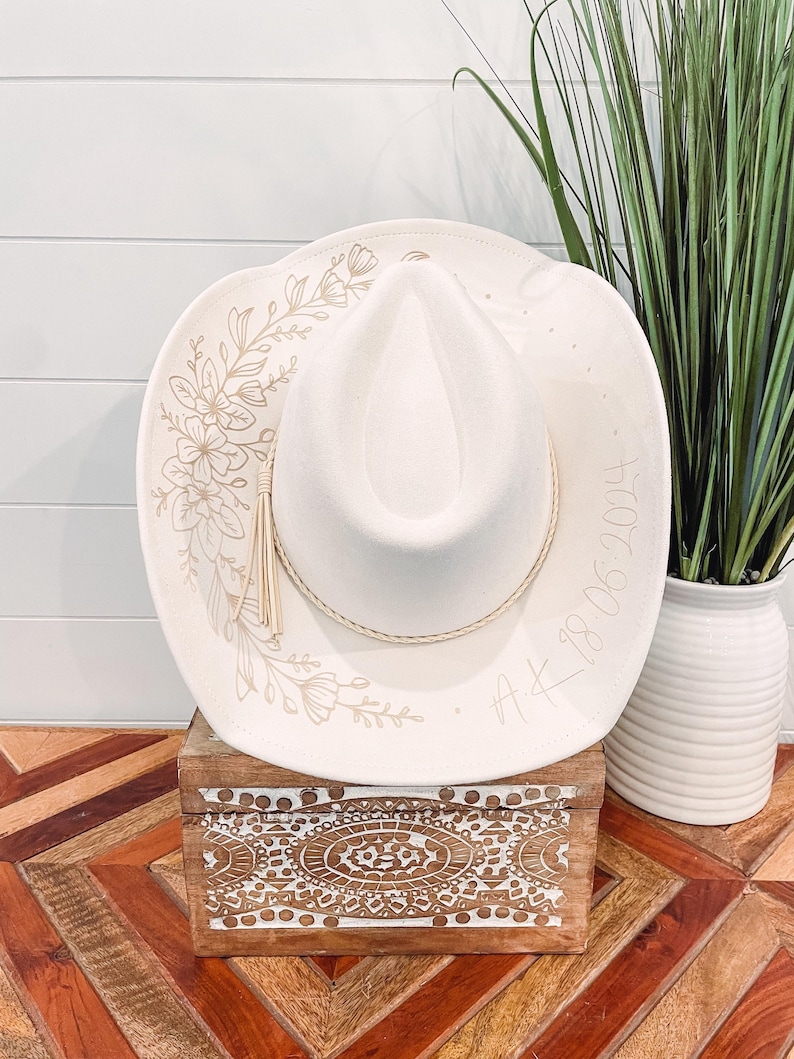 May include: A white cowboy hat with a floral design and the text "A.K. 18.06.2014" on the brim.