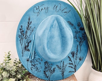 May include: A blue felt hat with a black floral design and the text "Stay Wild!" printed on the brim.