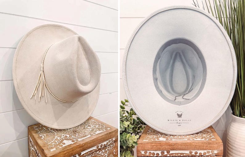 May include: A light gray felt fedora hat with a light brown leather band and a tassel. The hat has a  "Willie & Dolly Designs" logo on the inside.