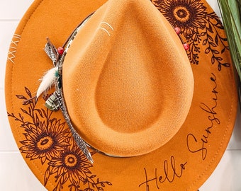 May include: A brown felt fedora hat with a black floral design and the text "Hello Sunshine" on the side.