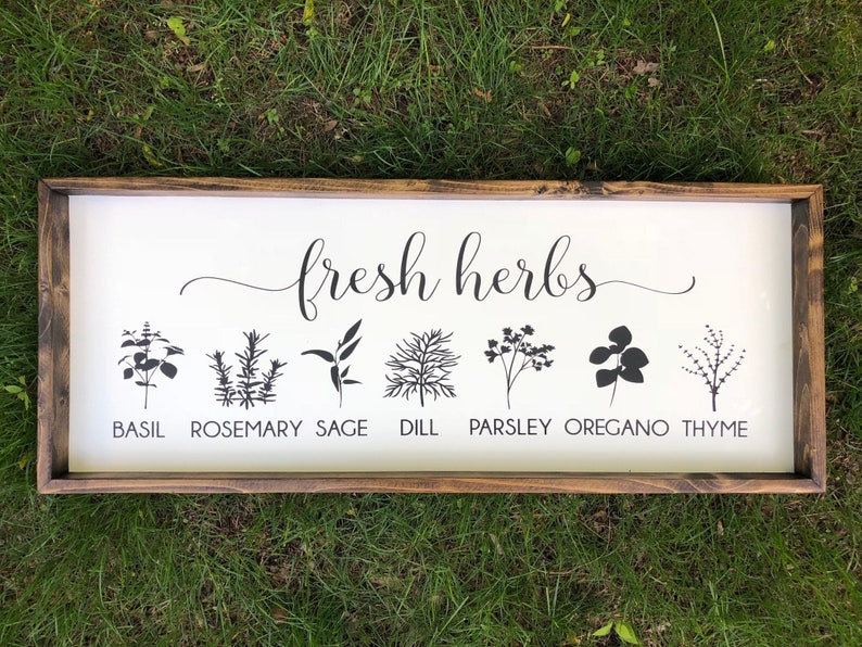 May include: A white wooden sign with the text "fresh herbs" in black cursive script. The sign features black silhouettes of various herbs, including basil, rosemary, sage, dill, parsley, oregano, and thyme, with their names printed below each silhouette.