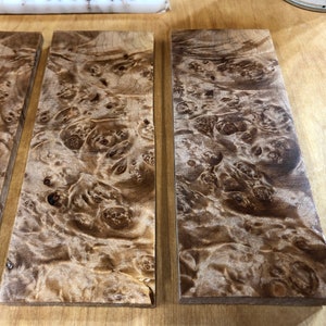 Pu&ograve; includere: Tre pezzi rettangolari di legno con un motivo a radica marrone e bianco. Il legno ha una finitura naturale e lucida.