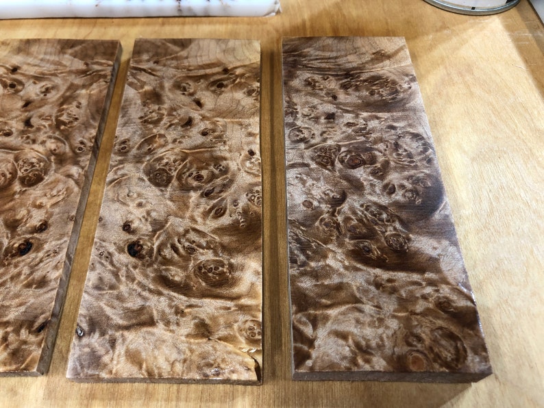 Pu&ograve; includere: Tre pezzi rettangolari di legno con un motivo a radica marrone e bianco. Il legno ha una finitura naturale e lucida.