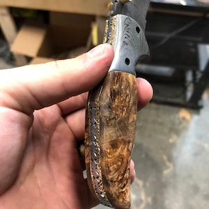 Pu&ograve; includere: Un coltello pieghevole con manico in legno e lama in acciaio damasco. Il manico &egrave; decorato con un intarsio in oro e argento.