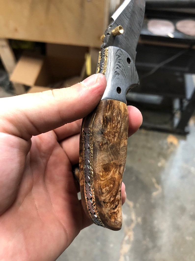 Pu&ograve; includere: Un coltello pieghevole con manico in legno e lama in acciaio damasco. Il manico &egrave; decorato con un intarsio in oro e argento.