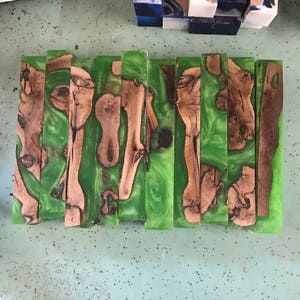 May include: Eight green and brown wood blanks with a swirl pattern. The blanks are arranged in a row.