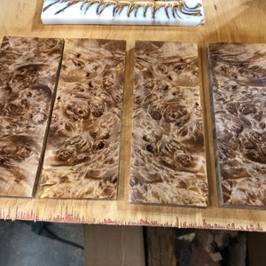 May include: Four rectangular pieces of wood with a brown and white burl pattern. The wood is arranged in a row on a light brown surface.