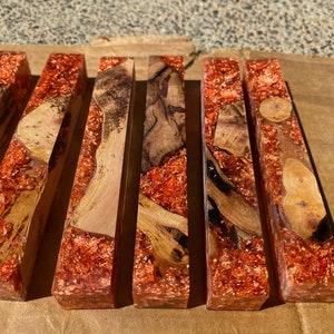 May include: A collection of rectangular resin blocks with embedded wood and copper flakes. The wood varies in color from light to dark brown, and the copper flakes add a shimmering, metallic effect. The blocks are arranged side by side.