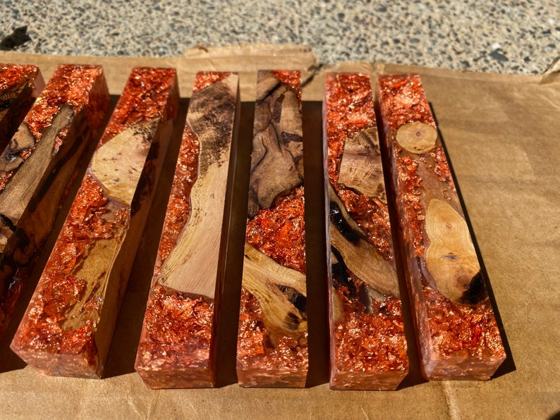 May include: A collection of rectangular resin blocks with embedded wood and copper flakes. The wood varies in color from light to dark brown, and the copper flakes add a shimmering, metallic effect. The blocks are arranged side by side.