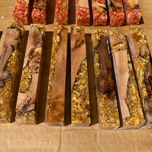 May include: Artisan-made resin blocks with embedded wood and gold leaf accents. The blocks feature a clear resin base, showcasing the natural wood grain and shimmering gold leaf. These decorative blocks are ideal for home decor or craft projects.