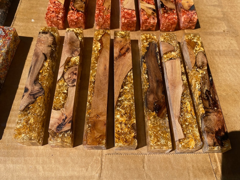 May include: Artisan-made resin blocks with embedded wood and gold leaf accents. The blocks feature a clear resin base, showcasing the natural wood grain and shimmering gold leaf. These decorative blocks are ideal for home decor or craft projects.