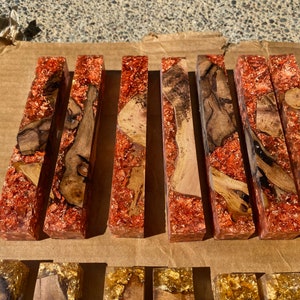 May include: A collection of rectangular resin blocks with embedded wood and copper-colored flakes. The wood pieces vary in shape and color, creating a unique contrast against the clear resin. These blocks are likely for crafting or decorative purposes.