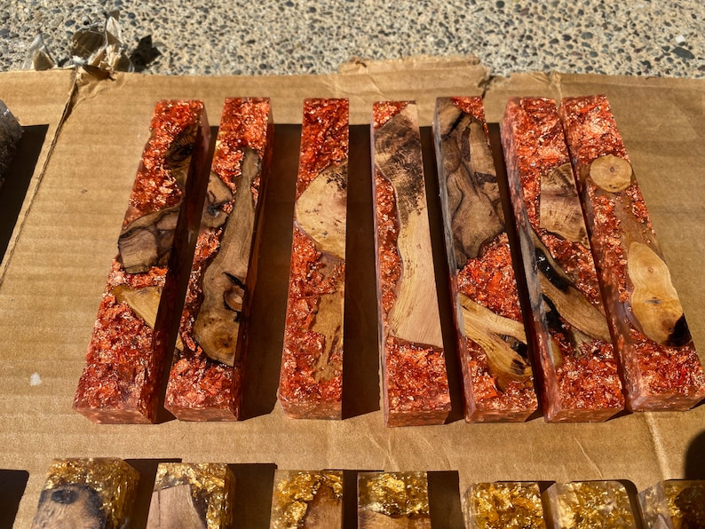 May include: A collection of rectangular resin blocks with embedded wood and copper-colored flakes. The wood pieces vary in shape and color, creating a unique contrast against the clear resin. These blocks are likely for crafting or decorative purposes.