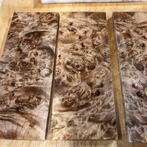Pu&ograve; includere: Tre pezzi di legno impiallacciato con un motivo a radica marrone e beige. Il legno ha una finitura naturale e lucida.