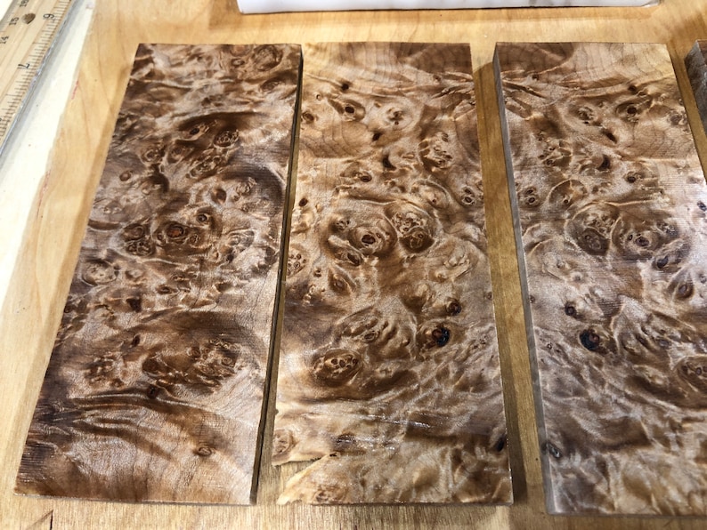 Pu&ograve; includere: Tre pezzi di legno impiallacciato con un motivo a radica marrone e beige. Il legno ha una finitura naturale e lucida.