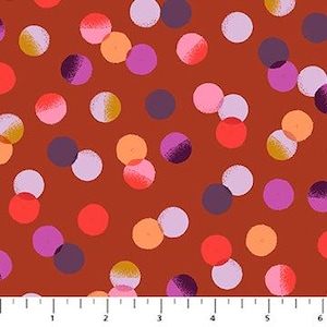 May include: Close-up of a fabric with a repeating pattern of colorful polka dots in shades of red, pink, purple, orange, and yellow on a rust-colored background. The dots vary in size and have a textured appearance. A ruler is at the bottom.