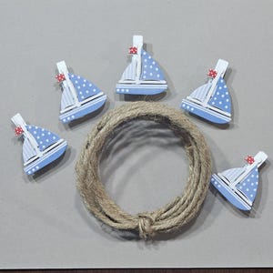 May include: Five blue and white sailboat-shaped clothespins with red accents. The clothespins are arranged in a circle around a ball of twine.