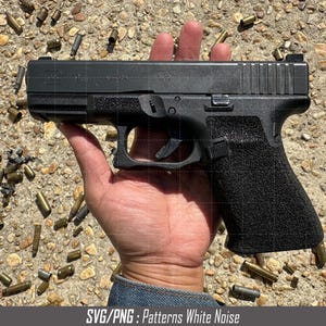 Puede incluir: Una pistola negra con un agarre texturizado, sostenida en una mano sobre un fondo de casquillos de latón dispersos.