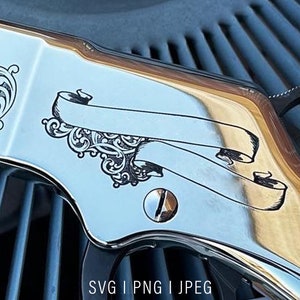 Könnte beinhalten: Nahaufnahme eines silbernen Gewehrs mit einem gravierten Design, das ein Rankenmuster und ein Banner mit einem leeren Platz für Text zeigt. Das Gewehr liegt auf einer blau-silbernen Oberfläche.