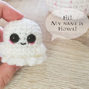 May include: A white crocheted ghost with black eyes and pink cheeks. The ghost is holding a speech bubble that says "Hi! My name is Howl!"