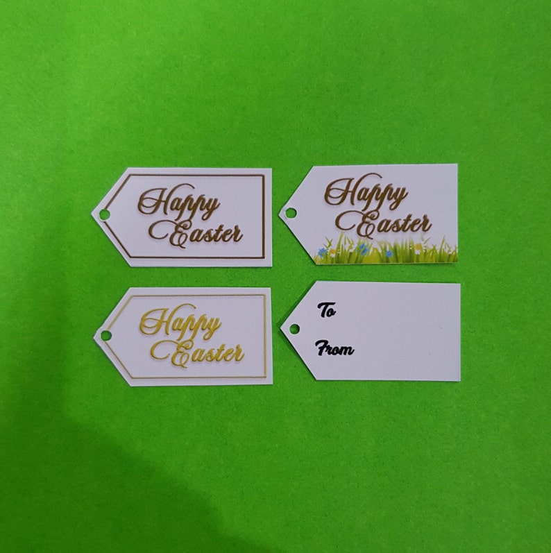 May include: Four white gift tags with a Happy Easter message. Two tags have a gold cursive font, one has a brown cursive font, and one has a brown cursive font with a green grass and blue flower design.