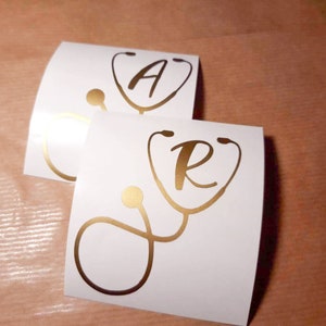 Peut inclure: Deux autocollants en vinyle blanc avec des lettres dorées et un design de stéthoscope doré. Le premier autocollant a la lettre "A" à l'intérieur du stéthoscope. Le deuxième autocollant a la lettre "R" à l'intérieur du stéthoscope.