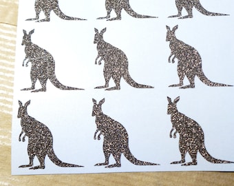 May include: A sheet of 12 silver glitter kangaroo stickers. The kangaroos are all facing the right and are in a silhouette style.