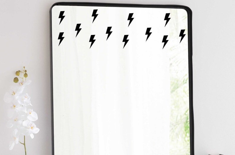 May include: A black framed mirror with multiple black lightning bolt decals on the surface.