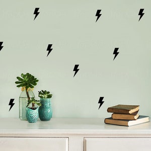 May include: A white dresser with two drawers, a stack of books, and two potted succulents. The wall behind the dresser is painted a light green color and decorated with black lightning bolt decals.