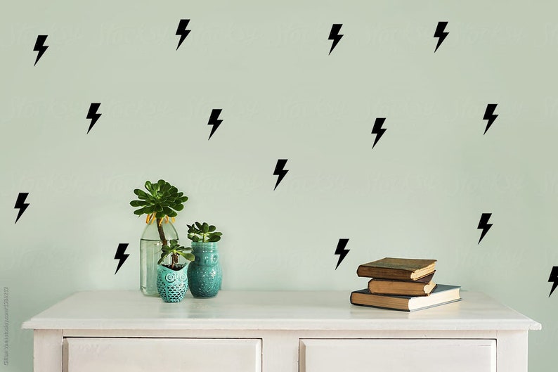 May include: A white dresser with two drawers, a stack of books, and two potted succulents. The wall behind the dresser is painted a light green color and decorated with black lightning bolt decals.