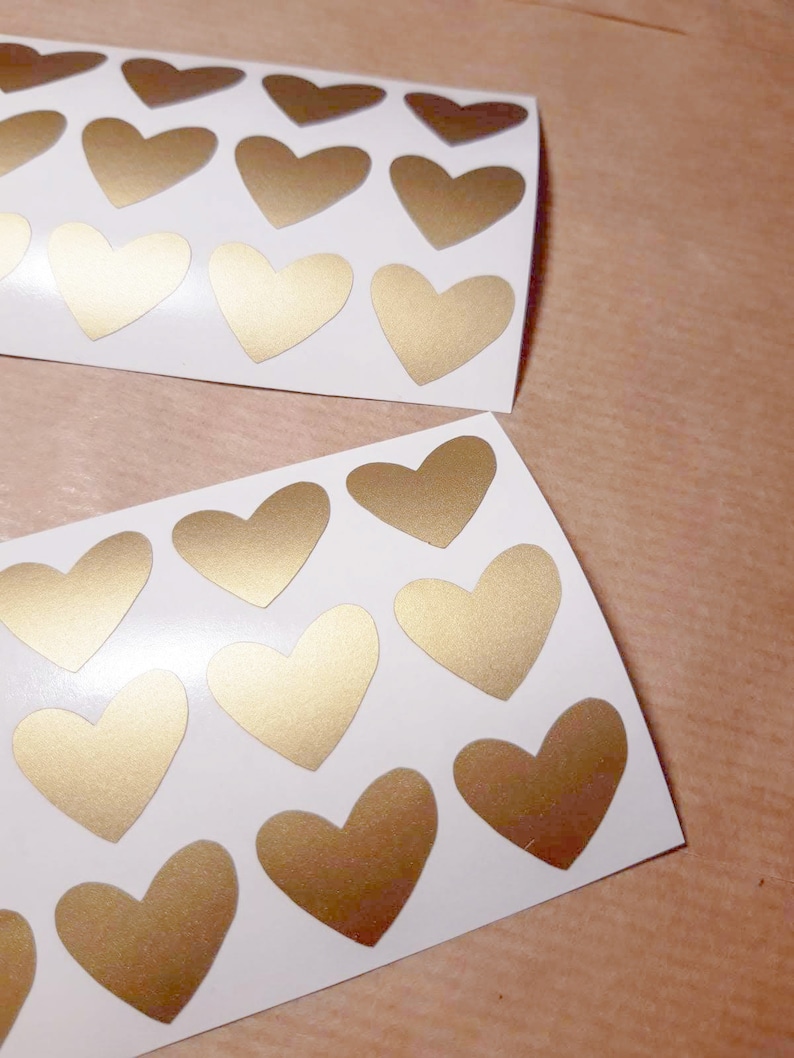 May include: Two sheets of white paper with gold heart stickers. Each sheet has 15 heart stickers.