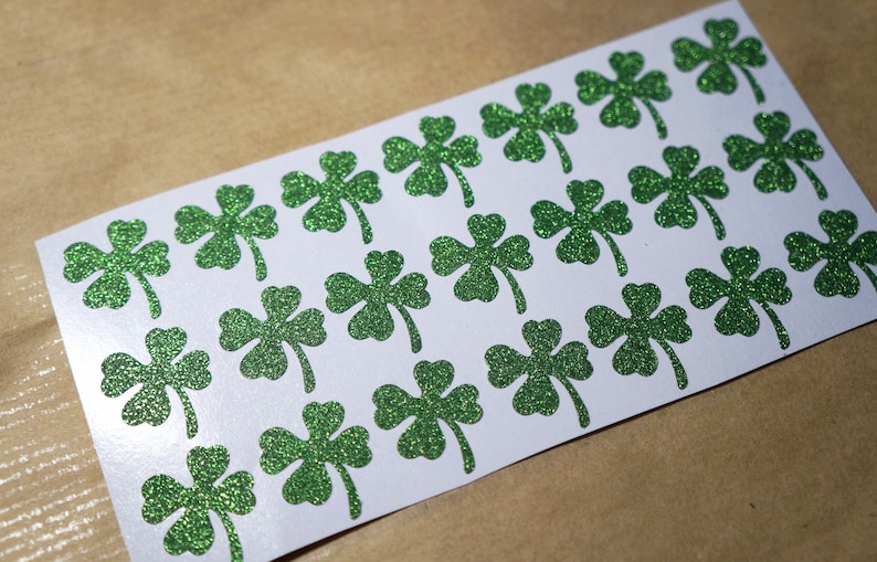 May include: A sheet of white paper with 20 green glitter shamrock stickers.