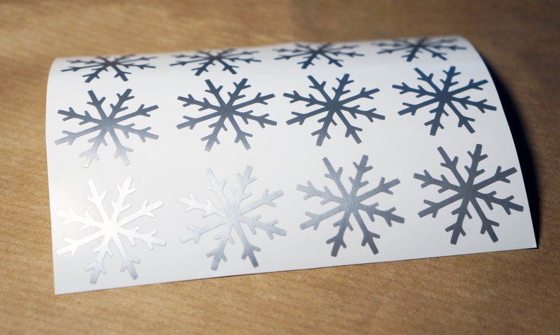 May include: A sheet of white paper with twelve silver snowflake stickers. The snowflakes are all the same design, with six points and a slightly textured surface.