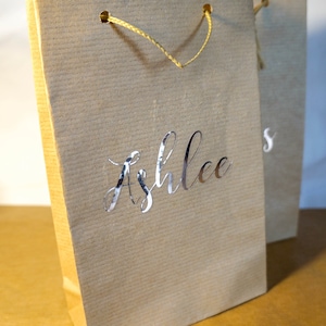 May include: A brown paper gift bag with a yellow rope handle and the name "Ashlee's" printed in silver foil.