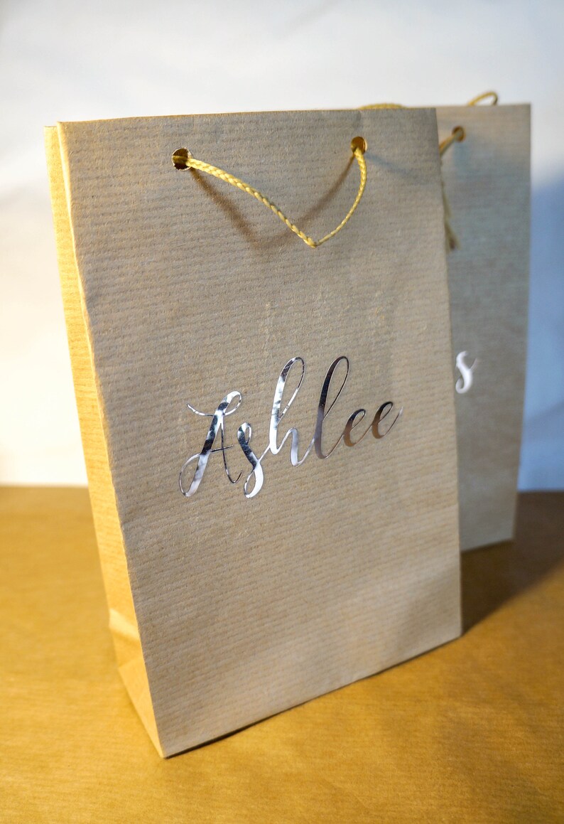 May include: A brown paper gift bag with a yellow rope handle and the name "Ashlee's" printed in silver foil.