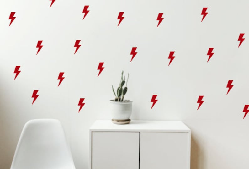 May include: A white wall with a repeating pattern of red lightning bolt decals. A small potted plant sits on a white shelf in front of the wall.