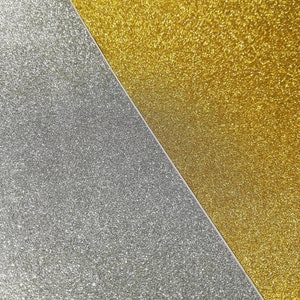 May include: A close-up of two pieces of glitter paper, one gold and one silver. The gold glitter paper is on the right side of the image and the silver glitter paper is on the left side of the image. The two pieces of paper meet in a diagonal line.
