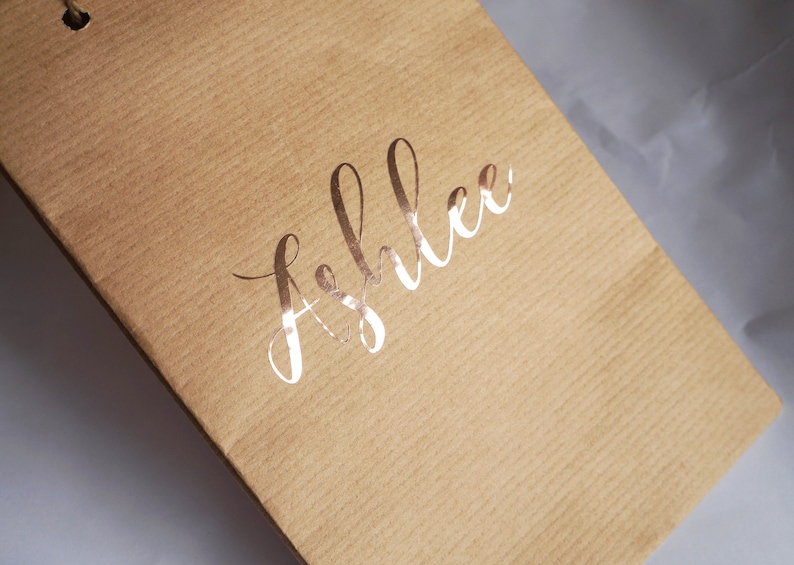 May include: A brown paper gift bag with the name "Ashlee" written in gold foil lettering.
