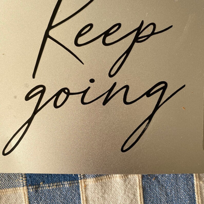 K&ouml;nnte beinhalten: Ein silberner Hintergrund mit den Worten "Keep going" in schwarzer Kursivschrift.