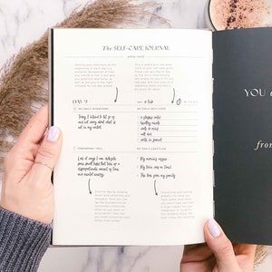 Op de afbeelding: Een zwart-wit dagboek met de titel "The Self-Care Journal" op de omslag. Het dagboek heeft een sectie voor dagelijkse intenties en dankbaarheid. Het dagboek is open op pagina 9, gedateerd 15 februari.