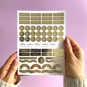 May include: Gold foil sticker sheet with various designs including hearts, bath tubs, and motivational phrases like "You Got This" and "Go With The Flow".