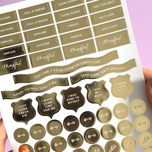 May include: Gold foil stickers with motivational phrases and images, including "Slow Down", "Ask for Help", "Self-Love", "Mindful", "You Can't Pour From an Empty Cup", "Good Things Take Time", "Self-Care Isn't Selfish", "I Was Kind to Myself", "I Did My Best", and "I Took Care of Me".