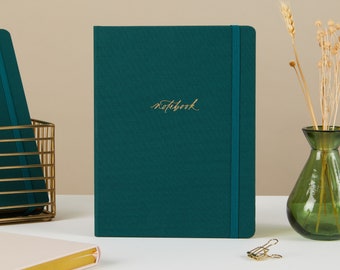 Puede incluir: Un cuaderno de color verde azulado con cierre elástico dorado y la palabra "notebook" escrita en letras doradas en la portada.