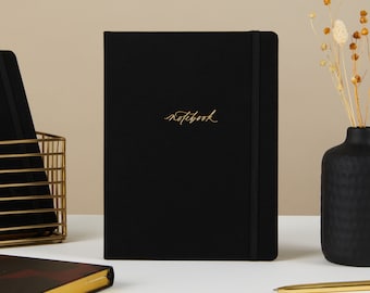 May include: A black notebook with a gold elastic closure and the word "notebook" written in gold script on the front cover.