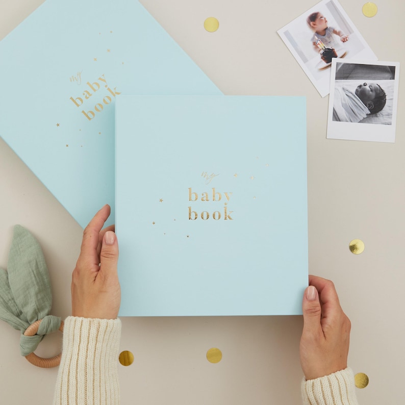 Aqua baby memory book with a light blue cover and elegant gold foiled details, designed as a keepsake record book for new parents. Inside are 114 guided pages with prompts and space to capture milestones from pregnancy through to age 5, including first words, first steps, birthdays, and family memories. This gender-neutral baby record book comes in a matching foiled presentation box, making it a thoughtful baby shower gift or newborn keepsake.