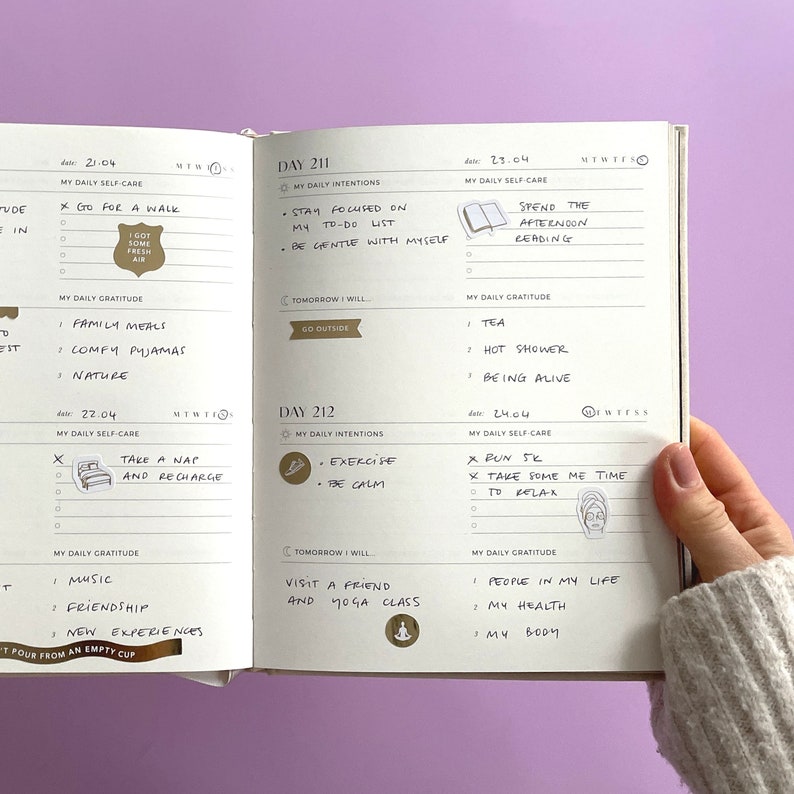 May include: An open journal with daily self-care and gratitude prompts. The journal is open to pages for April 21st and 22nd. The pages are filled with handwritten notes and stickers.
