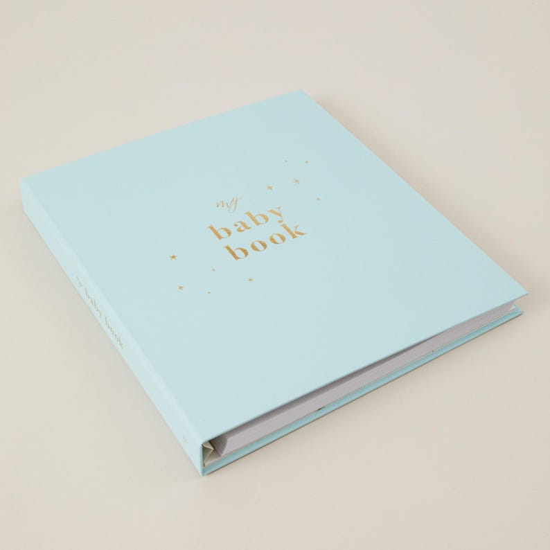 Light blue baby memory book with elegant gold foiled details on a light blue cloth cover. A gender-neutral baby journal featuring 114 pages of guided prompts to record special milestones such as pregnancy details, baby’s birth story, first steps, birthdays, and more. Plenty of space is included for photographs and personal notes, making this memory book a timeless keepsake. Comes with a luxury foiled presentation box, perfect as a baby shower gift."